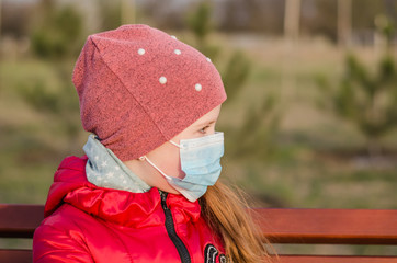 Baby girl in a medical mask in the park. Coronavirus protective mask. COVID-19