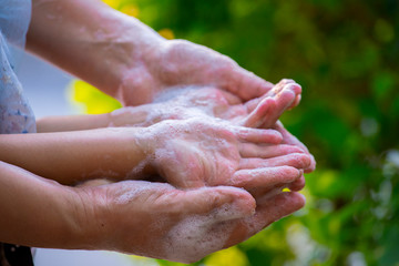Fototapeta premium Mother and child washing hands with soap and water on green blur background.