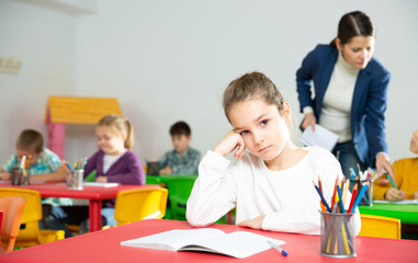 Upset schoolgirl sitting at a desk in classroom elementary school