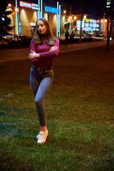 Photo of a cute teen girl one night in the light of the city lights of an outdoor building.