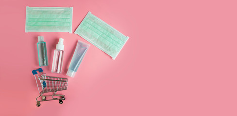 Small shopping cart and medical items to protect spread infectiously. Surgical mask, Alcohol gel and Alcohol spray on pastel pink background banner. Healthcare and shopping online concept, copy space