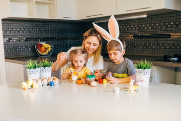 Happy easter! A mother and her daughter and son painting Easter eggs. Happy family preparing for Easter. Cute little child boy wearing bunny ears on Easter day.