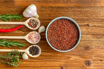 Brown rice, various of spices in spoons, and herbal on wooden background
