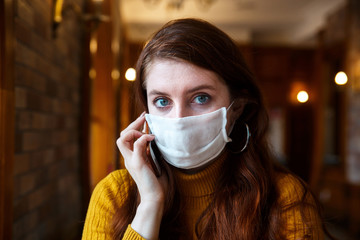 Young woman wearing a protective mask talking on a phone in cafe