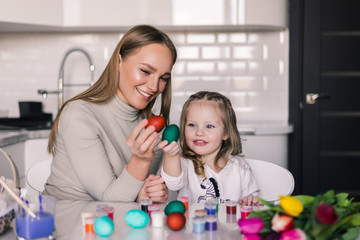 Mother and small daughter with easter eggs and easter basket in the kitchen ready for Easter