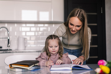 Young mother and child daughter doing homework writing and reading at home