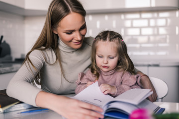 Obraz premium Young mother and child daughter doing homework writing and reading at home