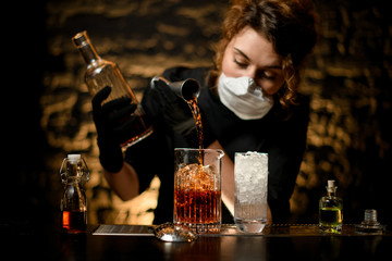 woman bartender in black clothes pours alcoholic drink into large glass with ice.