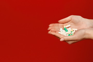 Various pills and capsules in female hands isolated at the red background. Healthcare and medicine concept
