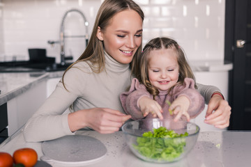 Mother and little girl slicing vegetables in the kitchen preparing a salad. Cook at home.