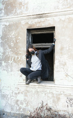 Fototapeta na wymiar A teenager girl in a black medical mask climbs through a window from an abandoned post-apocalyptic building. Consequences of COVID-19 Coronavirus protection. After a pandemic