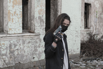 Teenager girl in a black medical mask with a children's gun, against the background of an abandoned post-apocalyptic building. Consequences of COVID-19 Coronavirus protection. After a pandemic