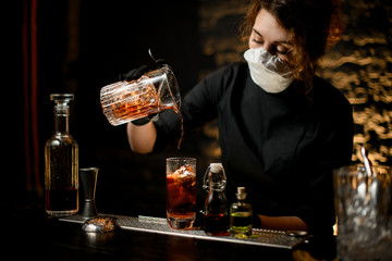 young woman at bar carefully pours cold cocktail into glass.