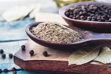 Ground black pepper in a spoon lies on a cutting board near the bay leaf and black pepper on a background of blue boards.