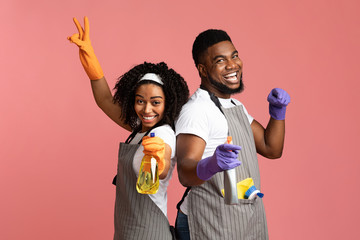 Cheerful african american couple with spray detergents posing on pink background - obrazy, fototapety, plakaty