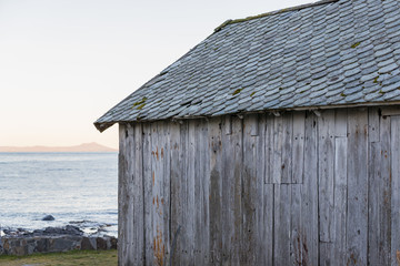 Old grey boat house with stone tiles on the roof.