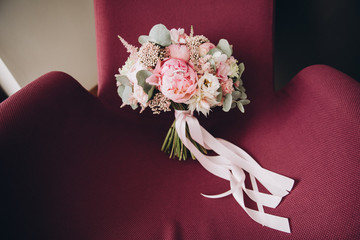 bouquet of white and pink flowers with greenery and a ribbon is in a red armchair