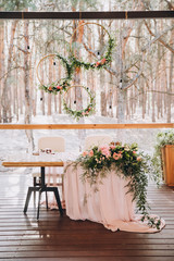 a banquet table with a pink tablecloth is decorated with a floral arrangement and stands against the backdrop of a pine forest