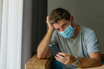 following online news on covid-19 virus pandemic - man with face mask in home quarantine lockdown checking internet information on the contagious disease worried - obrazy, fototapety, plakaty