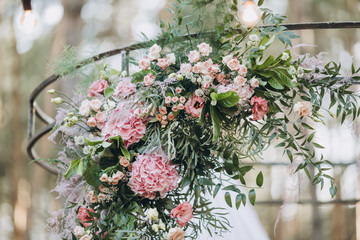 the arch for the wedding ceremony is decorated with floral arrangements and pink fabric and stands in a green meadow against the background of the forest