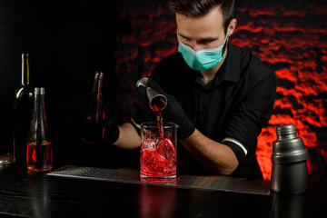 Bartender accurate pours alcoholic drink into large glass with ice.