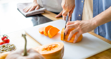 Man cutting fresh pumpkin on board on kitchen table