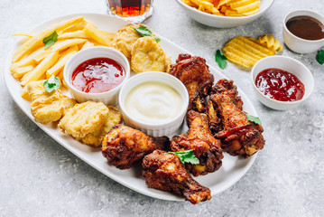 Table fof tasty snacks for beer prepared for watching sports on TV. Chicken. Chicken wings, chicken nuggets, french fries, chips, various sauces and lemonade. Light gray background. Selective focus