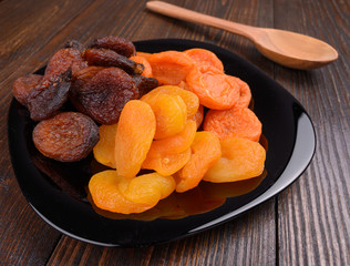 several types of dried apricots in a plate on a wooden background 