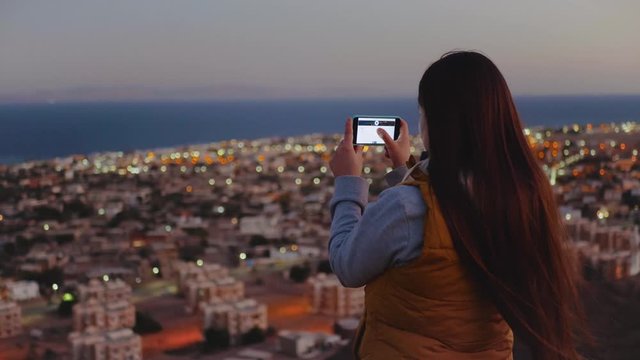 Woman take picture of the sea by smartphone in the evening. Woman stay on top of the mountain and looking Into Horizon, slow motion, 4k