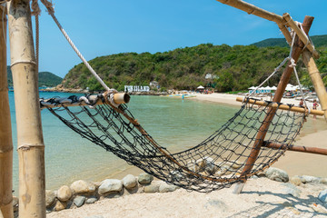 Obraz premium Bamboo hammock on a sandy beach and green hills in the tropics