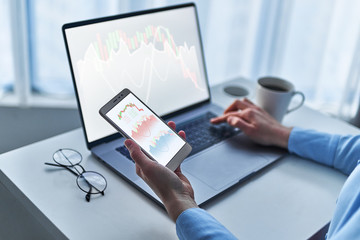 Modern business woman investor analyzes and watches a changing chart of stock trade and exchange money market on computer and smarthphone at workplace