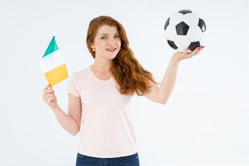 Young sports woman with a soccer ball and the flag of Ireland and looking at the camera. We play football and cheer for the country's national team.