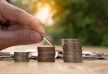 Saving money hand putting coins on stack on table with sunshine on nature background.