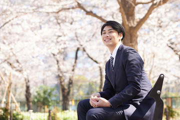 公園のベンチで笑顔で座る日本人男性ビジネスマン