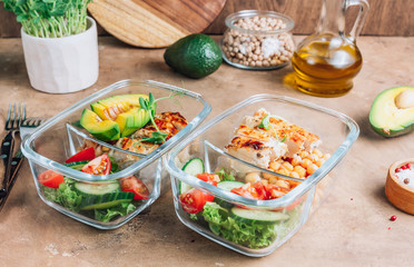 Healthy meal prep containers with chickpeas, chicken, tomatoes, cucumbers and avocados. Healthy lunch in glass containers on beige rustic background. Zero waste concept. Selective focus.