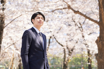 桜を背景に笑顔で立つ日本人男性ビジネスマン