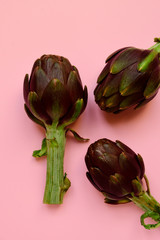 Obraz premium fresh artichokes on a pink background. layout top view. concept of seasonal vegetables. delivery of fresh vegetables