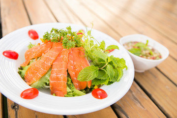 raw fresh salmon salad top with parsley decorated by mint and tomato in a white plate on wood table serve with thai style sause 