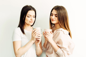 Two young girls girlfriends enjoy coffee, hold mugs in their hands on a white background