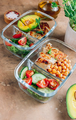 Healthy meal prep containers with chickpeas, chicken, tomatoes, cucumbers and avocados. Healthy lunch in glass containers on beige rustic background. Zero waste concept. Selective focus.