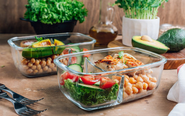 Healthy meal prep containers with chickpeas, chicken, tomatoes, cucumbers and avocados. Healthy lunch in glass containers on beige rustic background. Zero waste concept. Selective focus.
