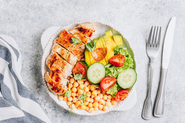 Healthy vegetable buddha bowl lunch with grilled chicken and chickpeas, cucumber, tomato and avocado on light gray background. Top view. Zero waste concept