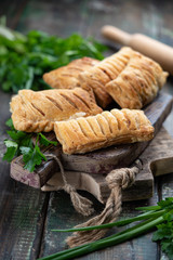 Baked puff pasrty with different fillings and herbs on wooden old fashion cutting board on dark wooden background. Macro, closeup