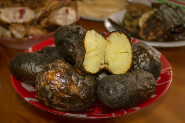 baked potatoes on the grill in a red plate on the background of grilled meat and vegetables