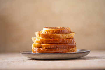 Fried croutons or egg toasts in a ceramic plate for morning coffee on an isolated light beige background. Stack of French toasts for breakfast. horizontal format