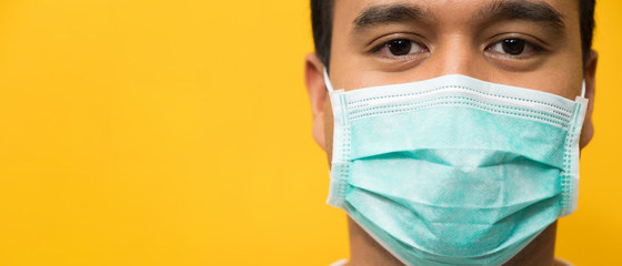 Close up young asian man wearing protection face mask against coronavirus on yellow background.