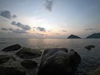 Sunset at the beach with stones in the ocean in Ko Tao Thailand with the island Koh Nang Yuan in...