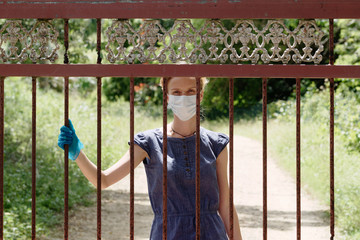 A woman in a medical mask and latex gloves closed the gate to the coronavirus quarantine. countryside