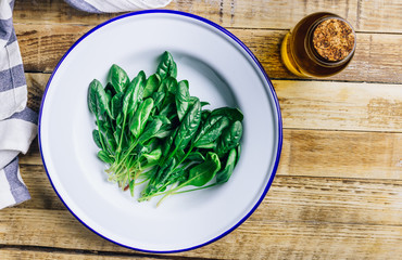 Fresh green baby spinach on plate on wooden rustic table. Healthy diet, vegetarian food concept.