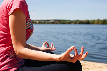 Fototapeta na wymiar Young girl meditating by the beautiful lake. Lotus Pose. Close-up.